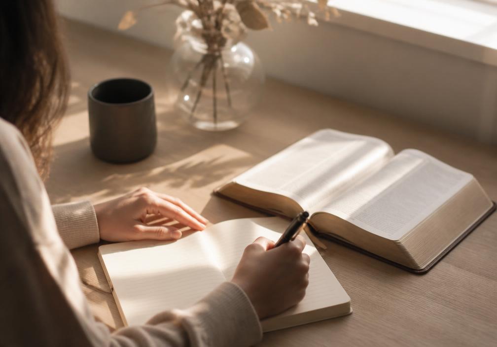 Mãos escrevendo em um caderno ao lado de uma Bíblia aberta